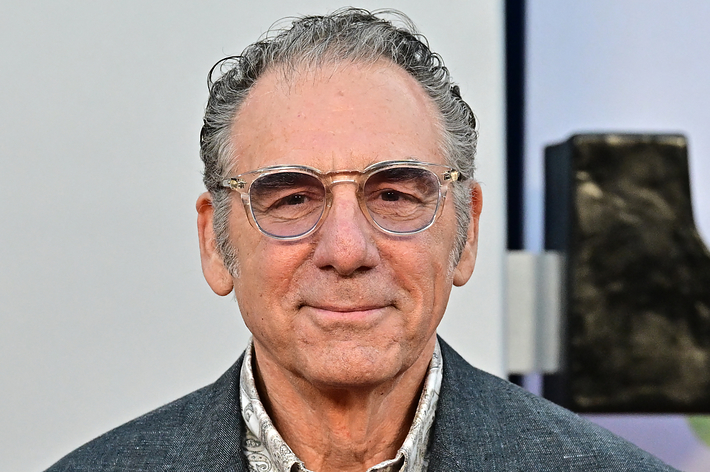 An older man with glasses and a patterned shirt smiles at the camera