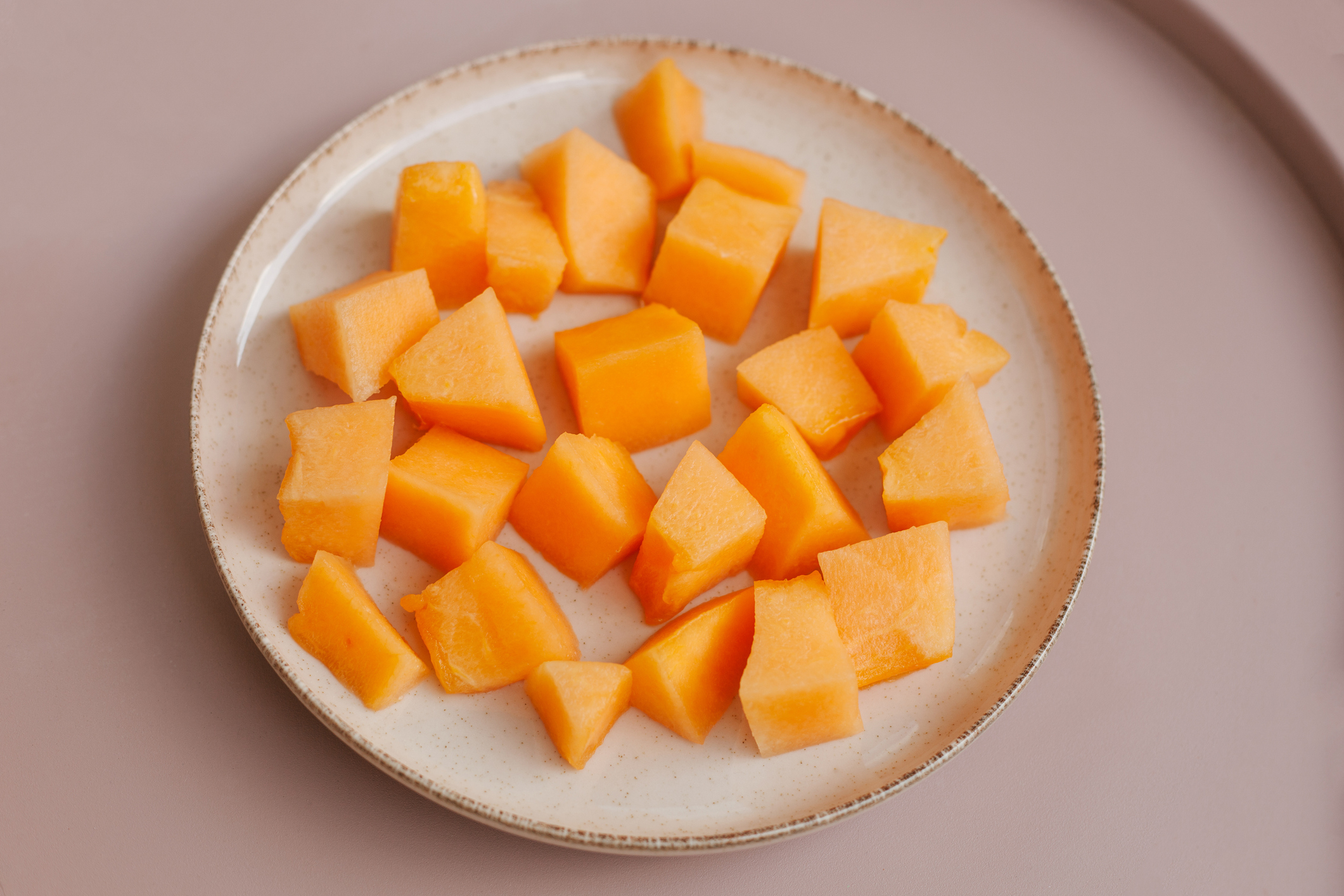 A plate of neatly arranged cubed cantaloupe on a light ceramic dish