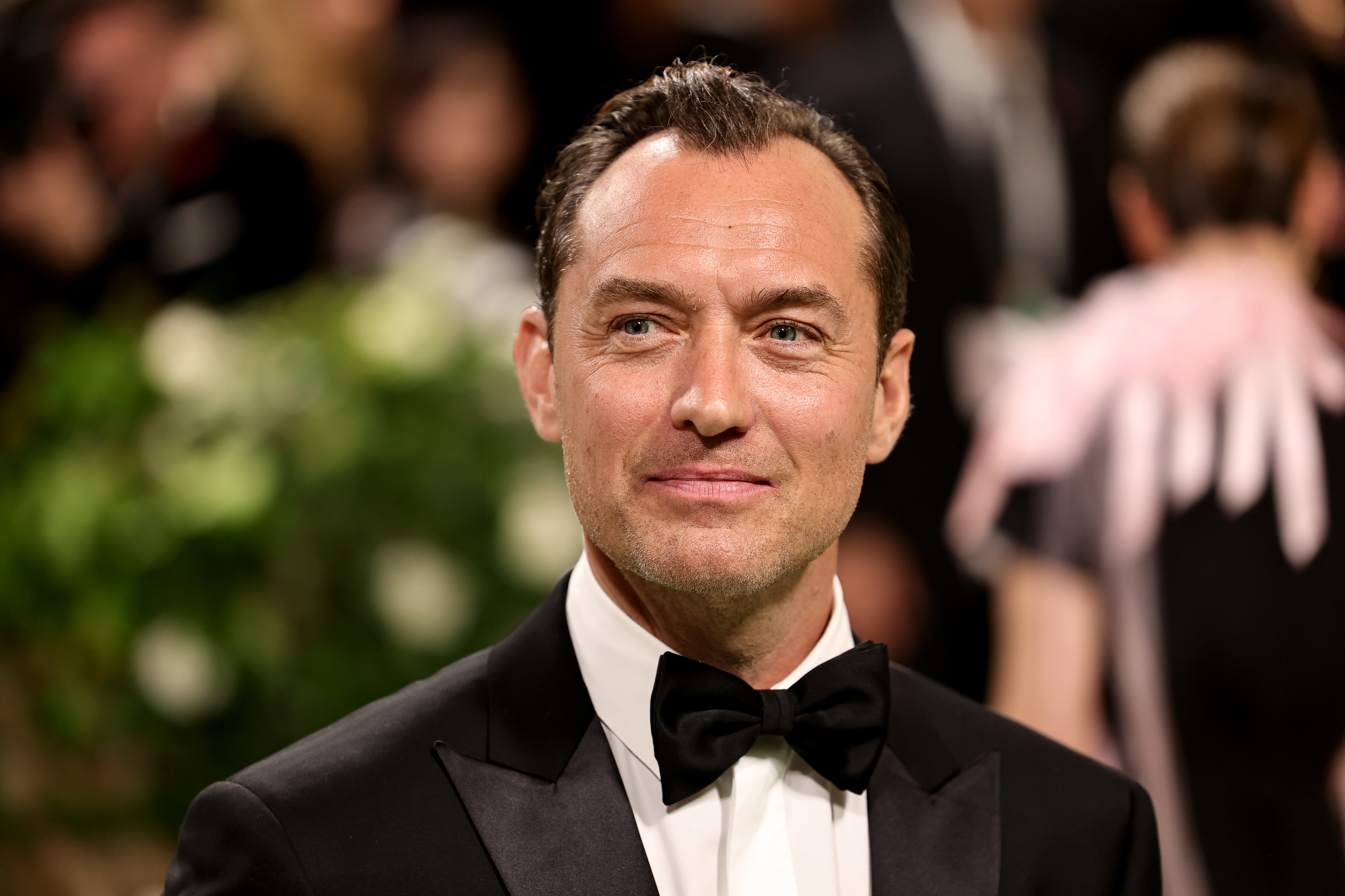 Jude Law at a formal event, wearing a classic black tuxedo with a black bow tie, smiling