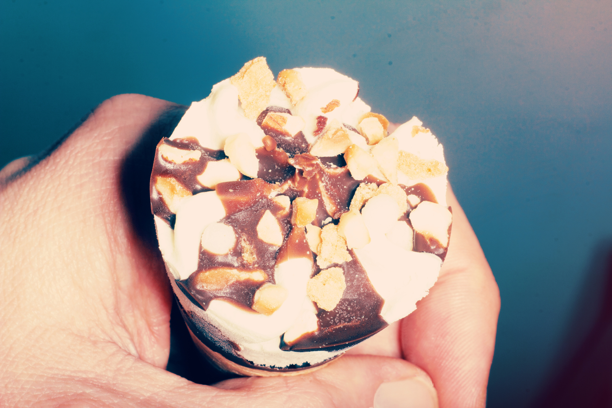 A hand holds a frozen dessert cone topped with peanuts, chocolate sauce, and vanilla ice cream