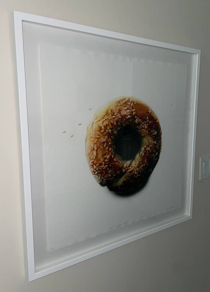 A framed picture of a sesame seed bagel with a white background, hanging on a wall