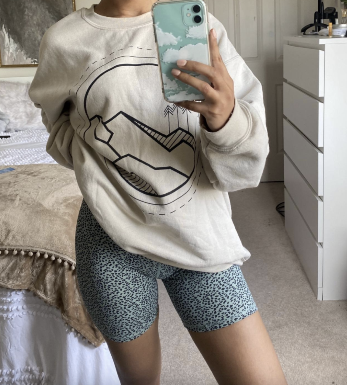 Person taking a mirror selfie in a casual outfit: an oversized sweatshirt with a geometric design and leopard print biker shorts. Their face is not visible