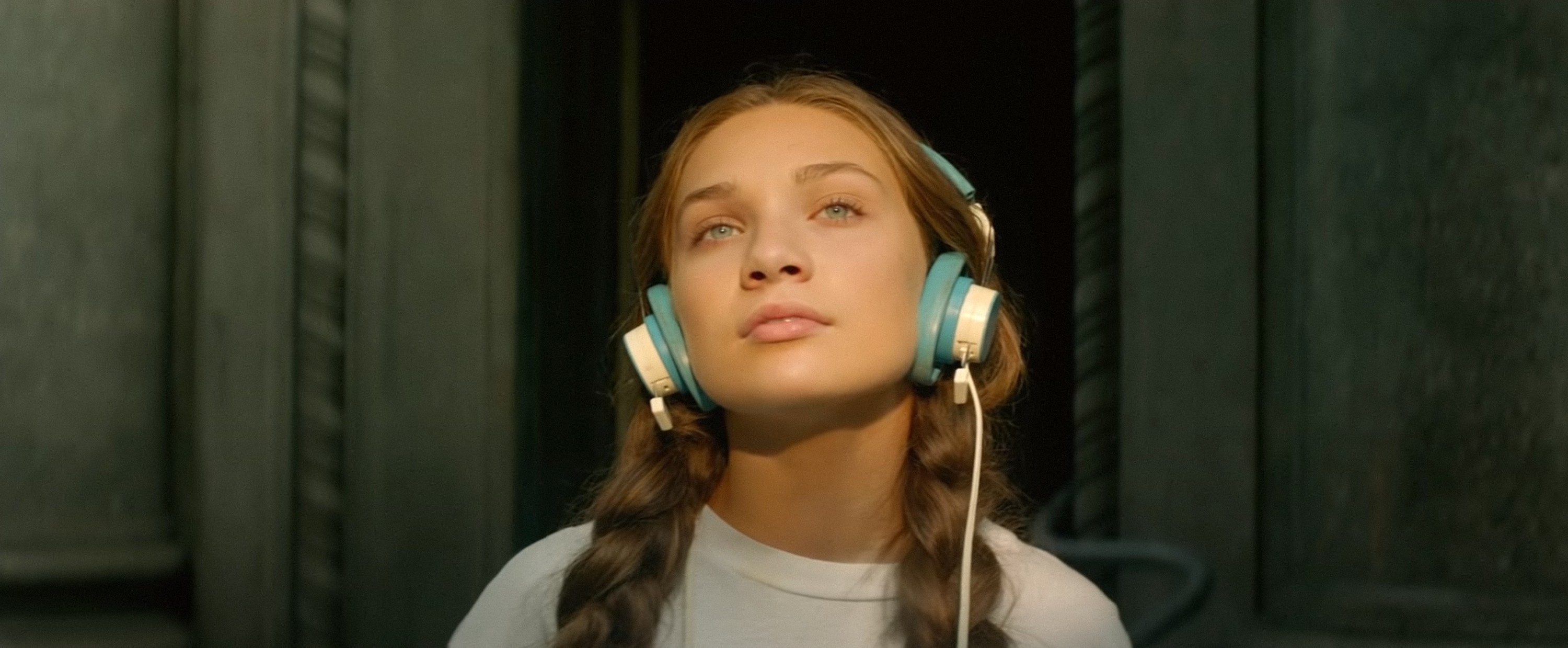 in a scene, Maddie with pigtail braids and headphones looks up contemplatively