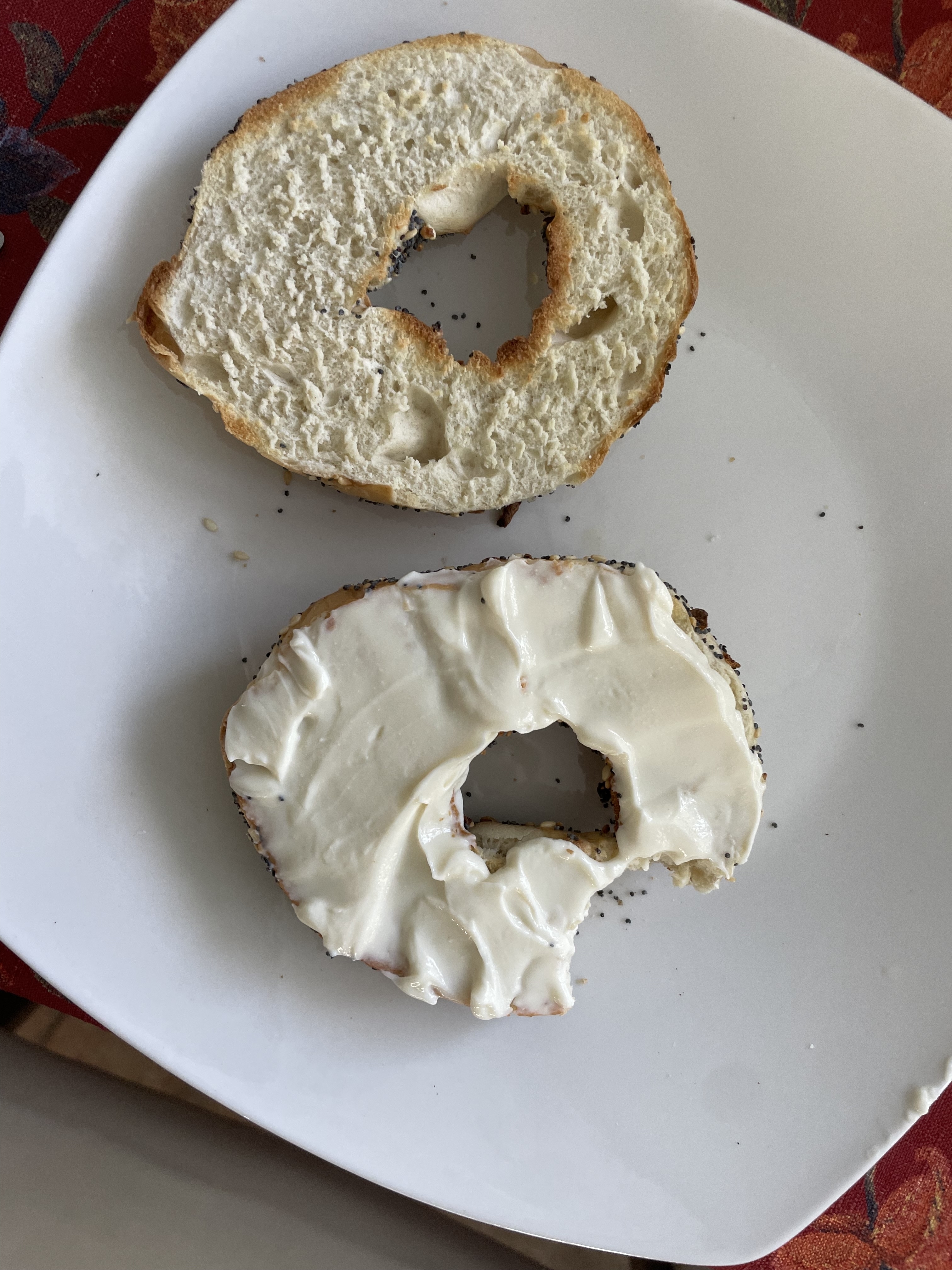 A split, toasted bagel on a white plate. One half is plain, and the other is spread with cream cheese