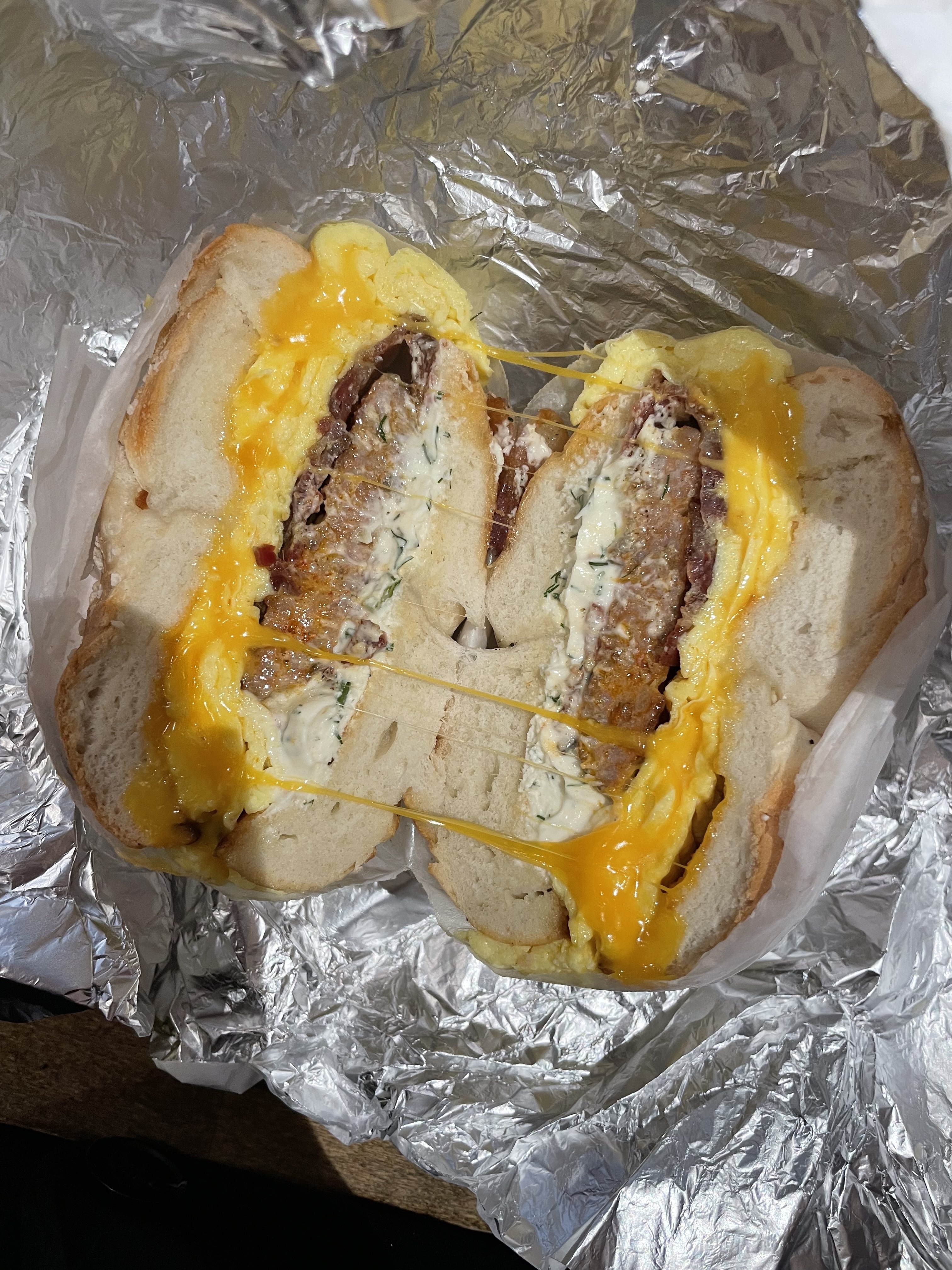 A close-up of a sandwich cut in half, featuring melted cheese and a patty, wrapped in foil
