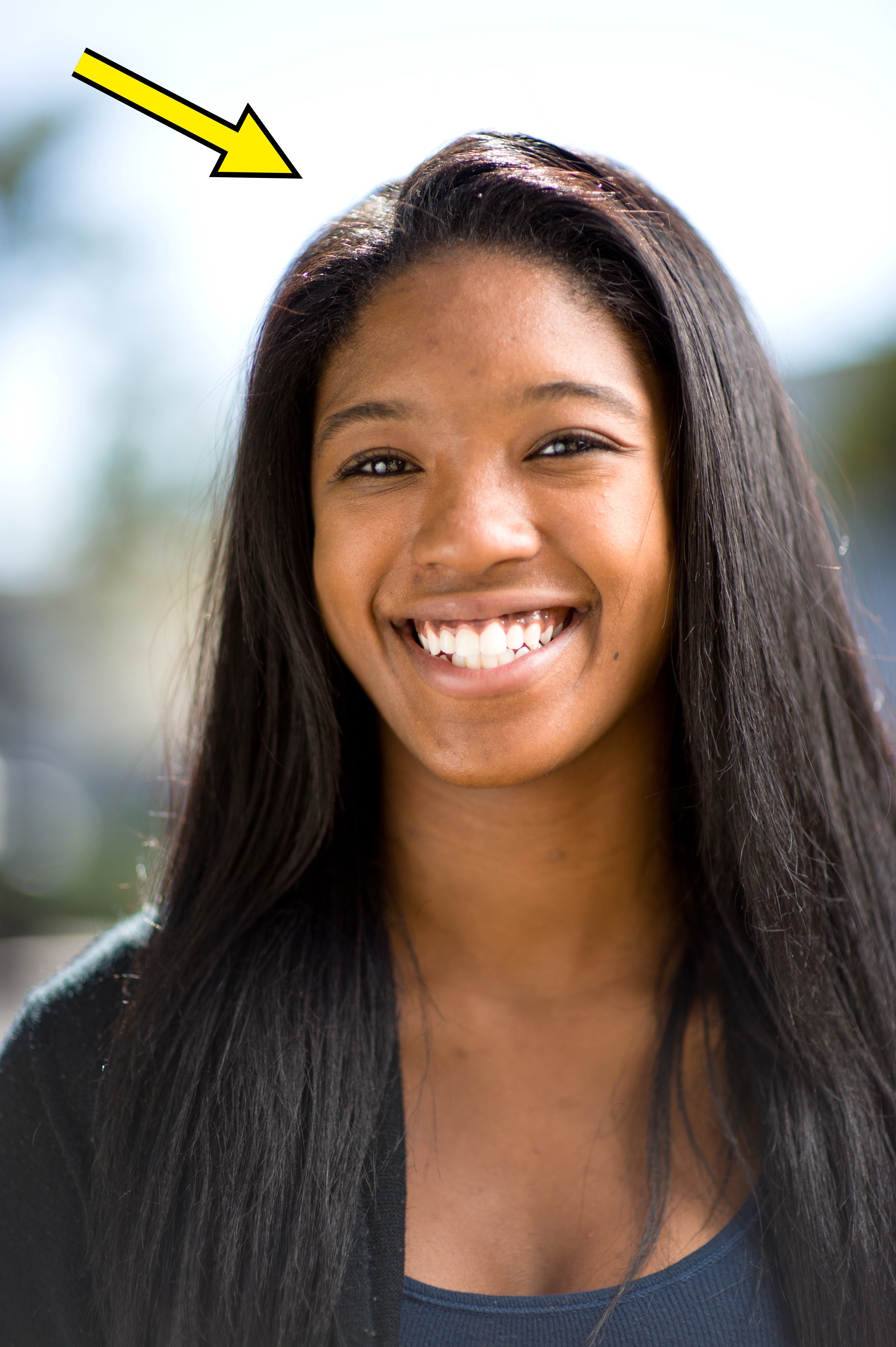A person with long hair smiling directly at the camera with a blurred background. Name not known