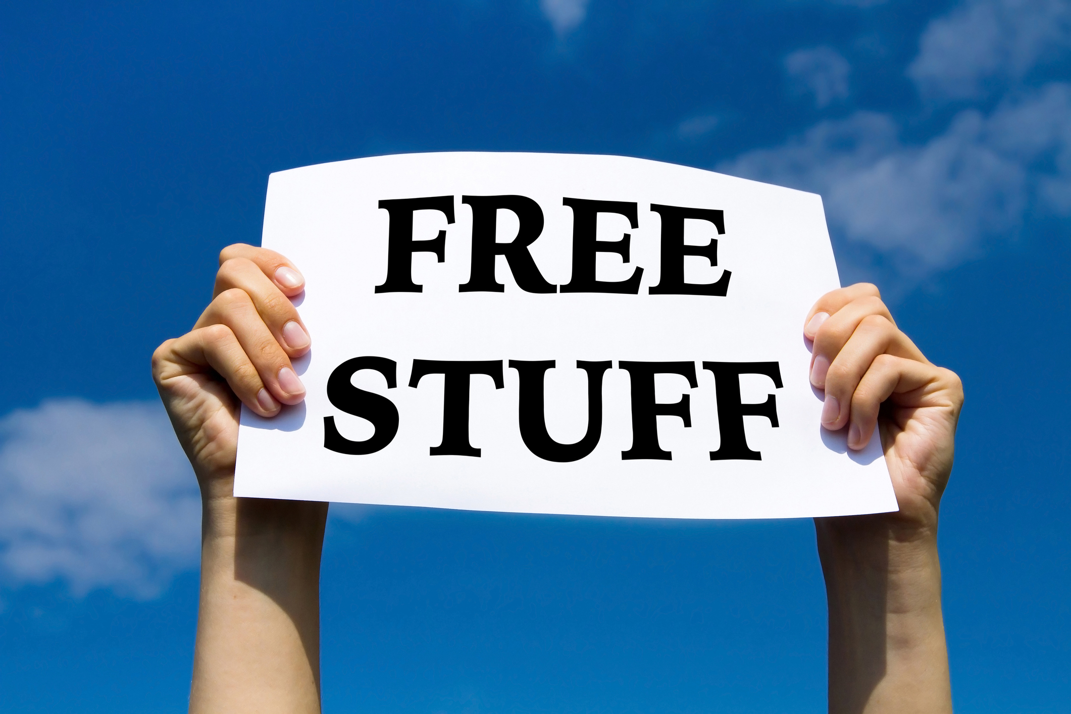 Hands holding a paper sign reading &quot;FREE STUFF&quot; against a blue sky