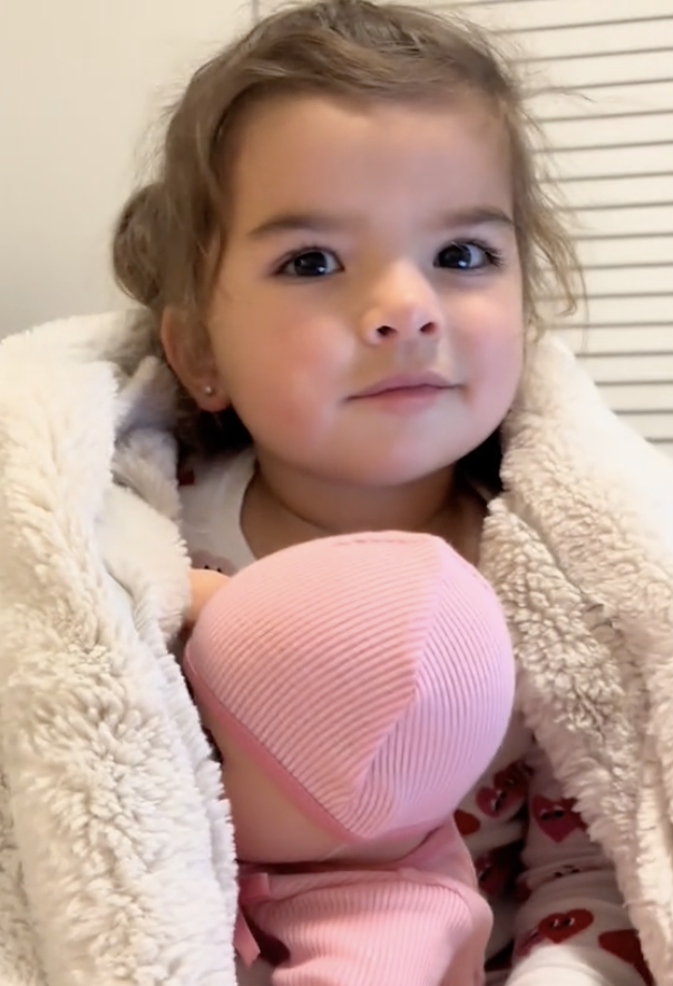 A young child is wrapped in a fluffy blanket, holding Baby
