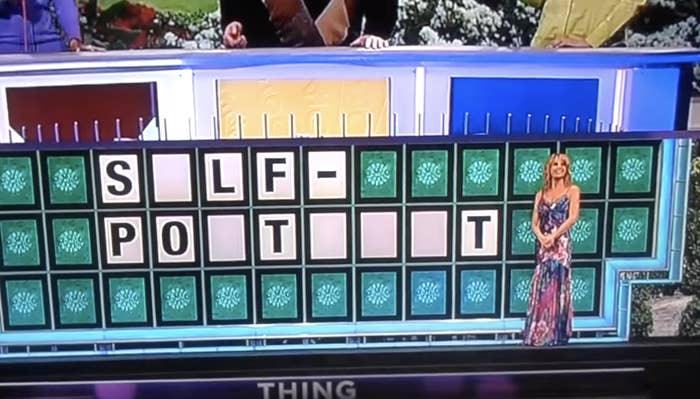 Vanna White stands next to a "Wheel of Fortune" puzzle board with the partially revealed phrase: "SELF-POT IT." The category is "THING."