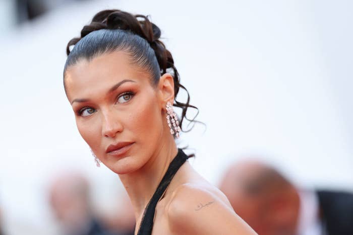 Bella Hadid on the red carpet, wearing elegant drop earrings and a gown with her hair styled in an updo. She is looking to the side