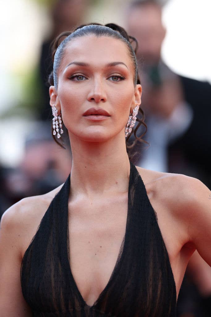 Bella Hadid on the red carpet wearing a black deep V-neck halter dress and chandelier earrings
