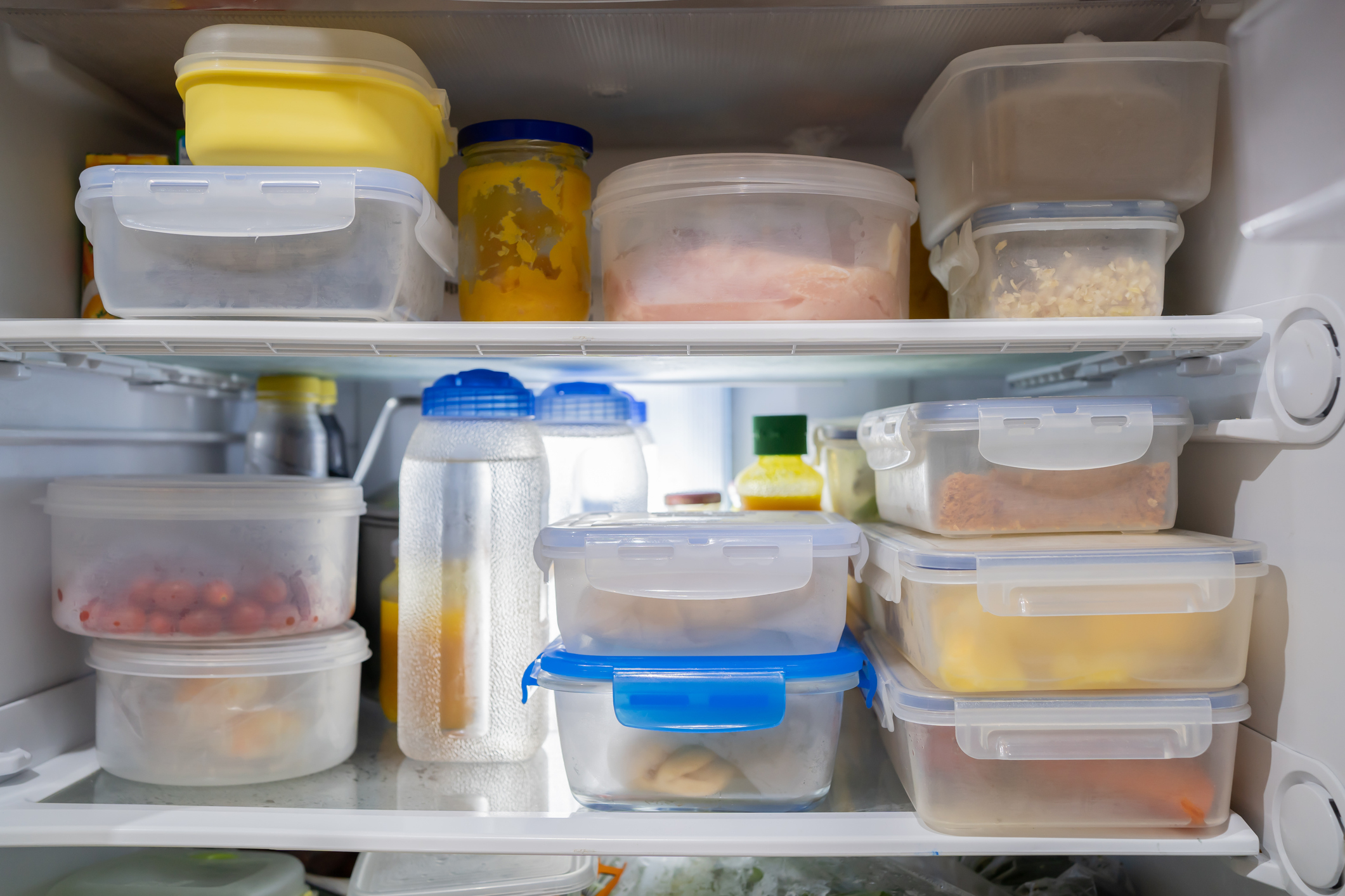 Et kjøleskap fylt med diverse plastbeholdere som inneholder forskjellige matvarer, inkludert rester, frukt og væsker