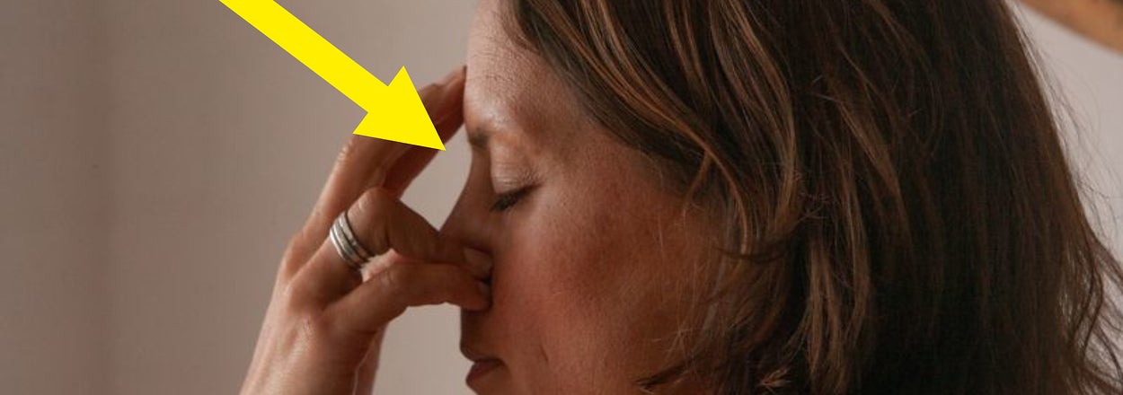 A woman is shown in profile with her eyes closed, touching her forehead with her fingers in a gesture. A yellow arrow points to her face