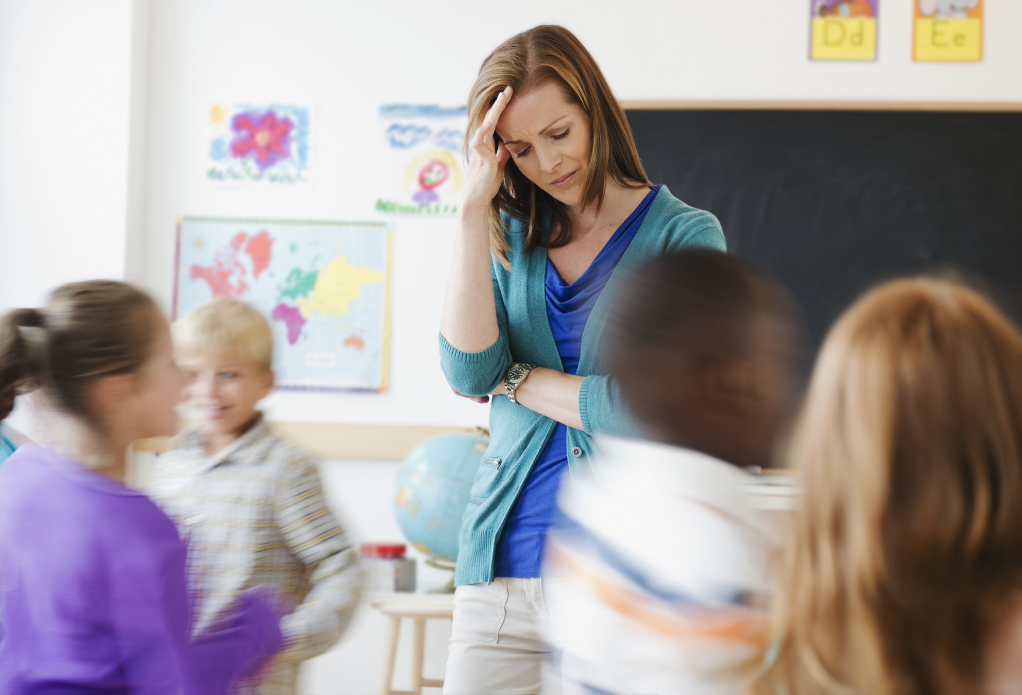 Teacher looks stressed while children play energetically in a classroom