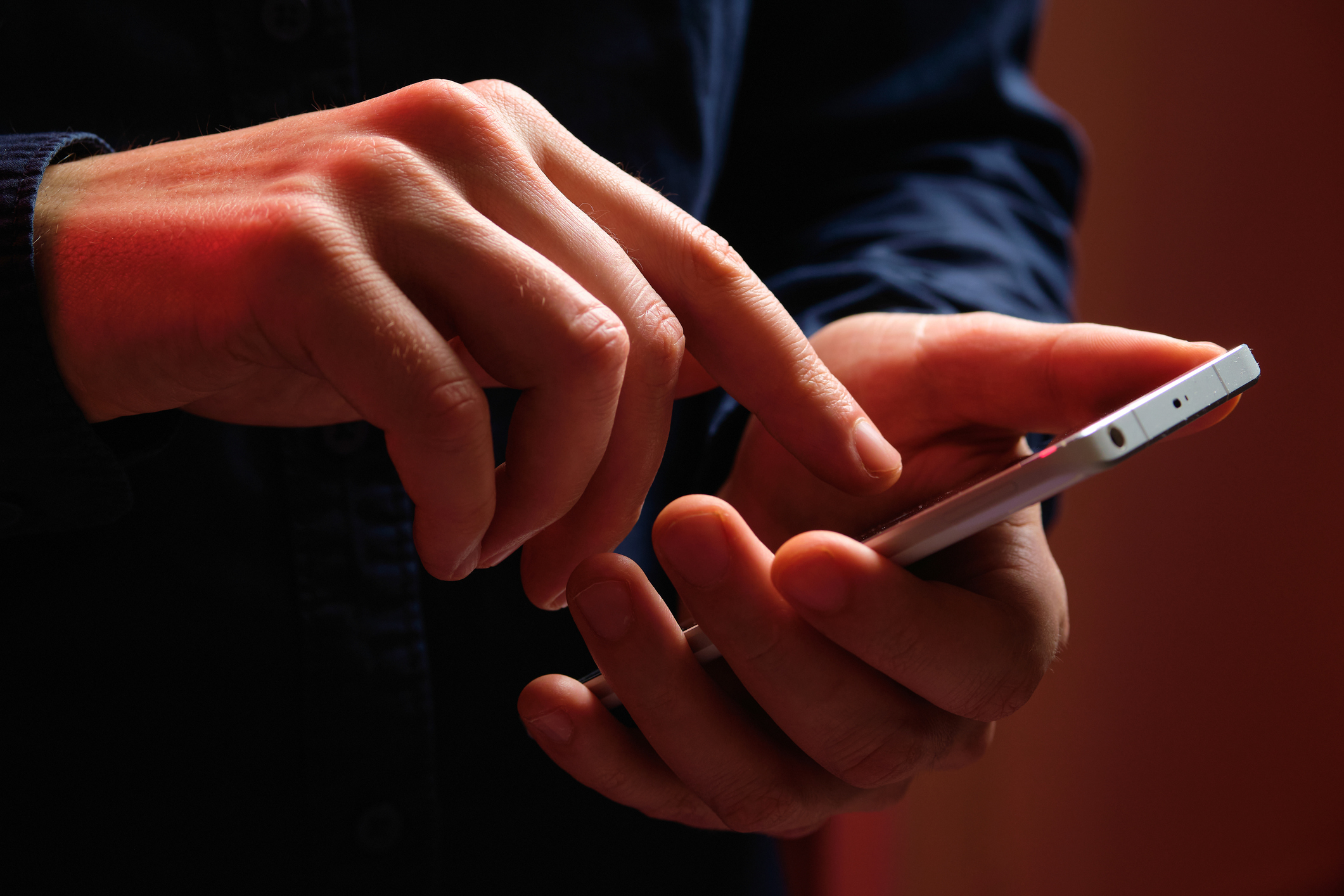 Close-up image of an adult&#x27;s hands using a smartphone, tapping and scrolling on the screen