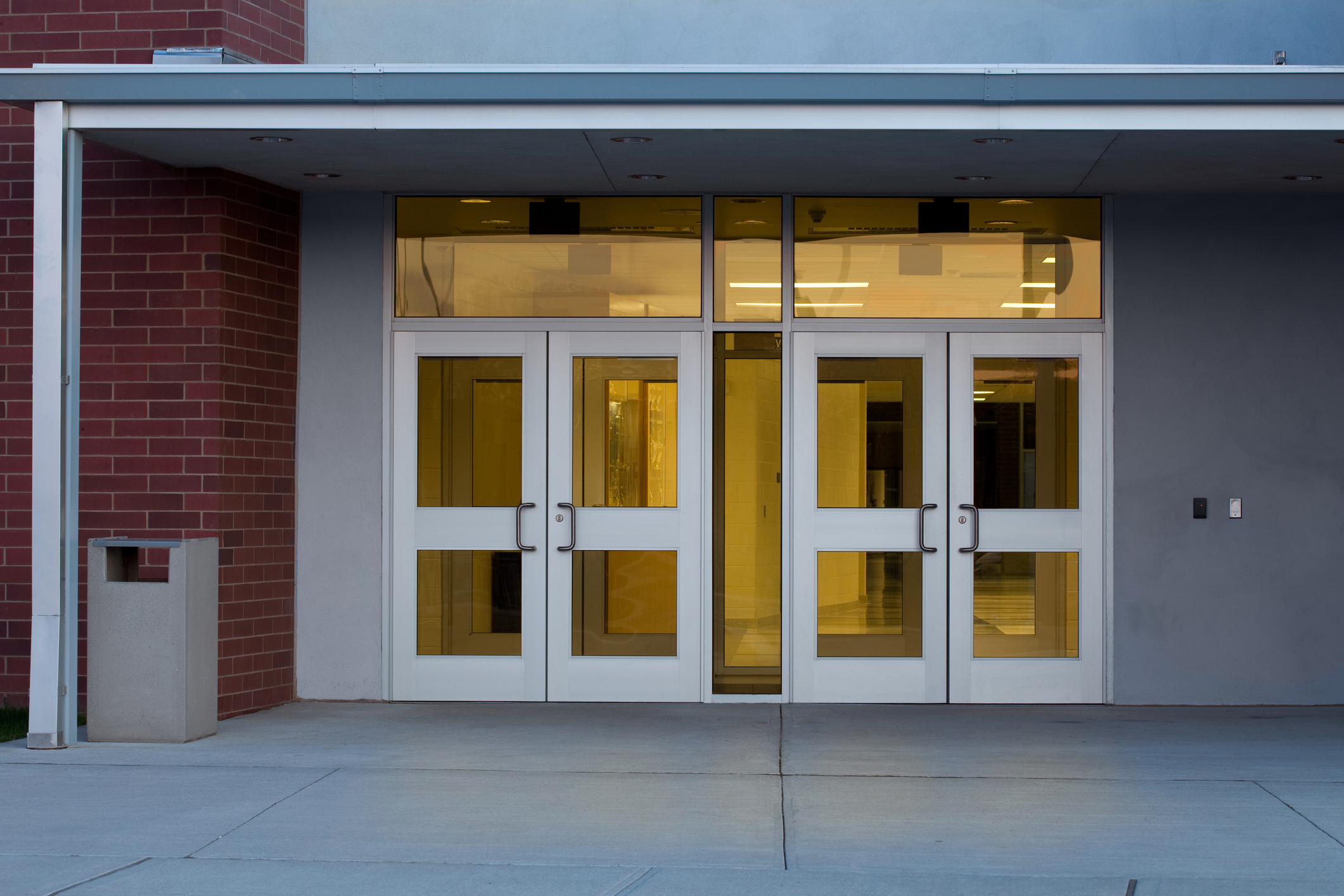 Entrance to a modern building with four glass doors and a brick wall on the left, with no people present
