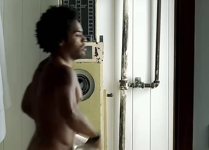 Donald Glover in a bare room with industrial pipes behind him, holding a towel