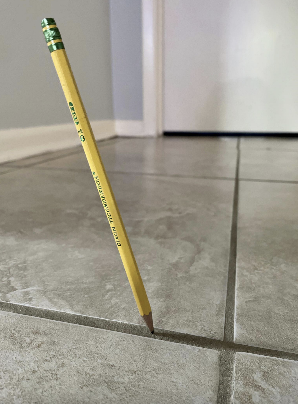 A pencil stands upright in the narrow gap between two tiles in a room with closed doors