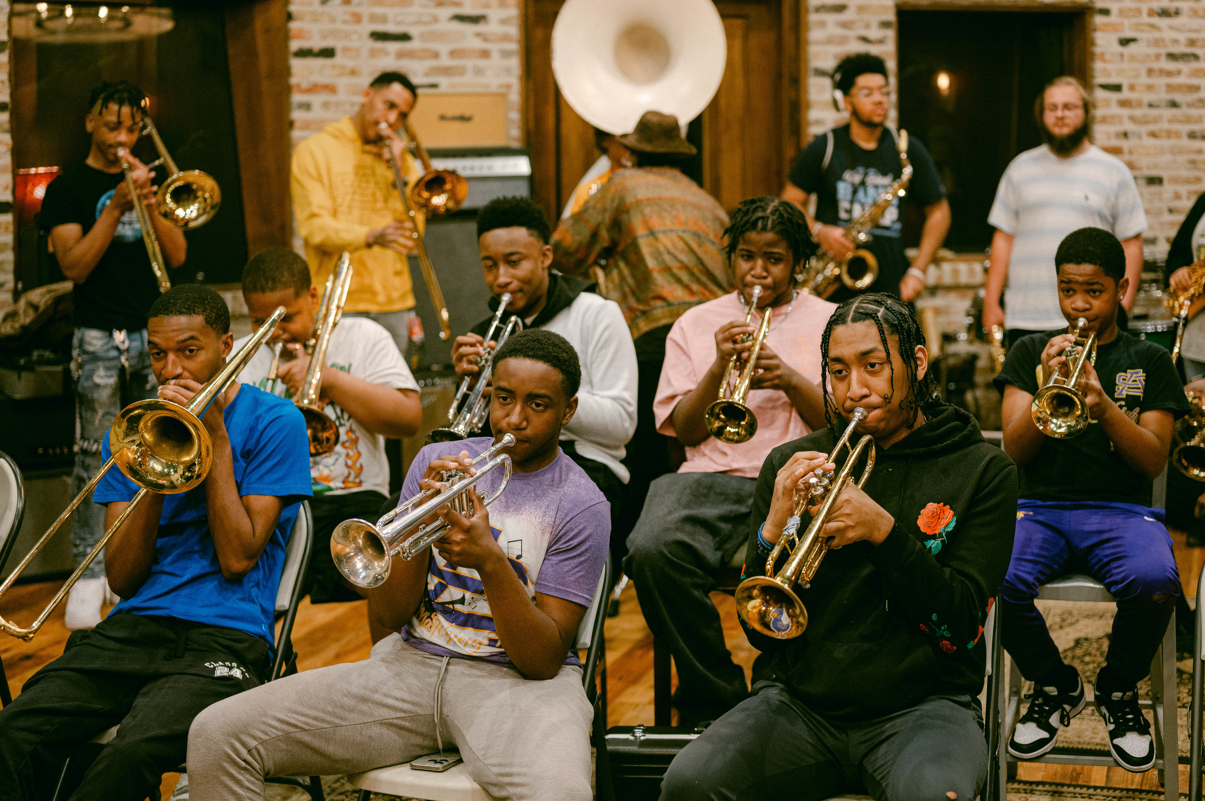A group of young musicians practice in a room, each playing brass instruments such as trumpets and trombones. A music practice session is underway