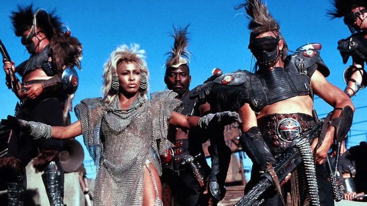 Tina Turner y un grupo de personas con trajes post-apocalípticos con espaldas y pinchos, en una escena de "Mad Max Beyond Thunderdome"