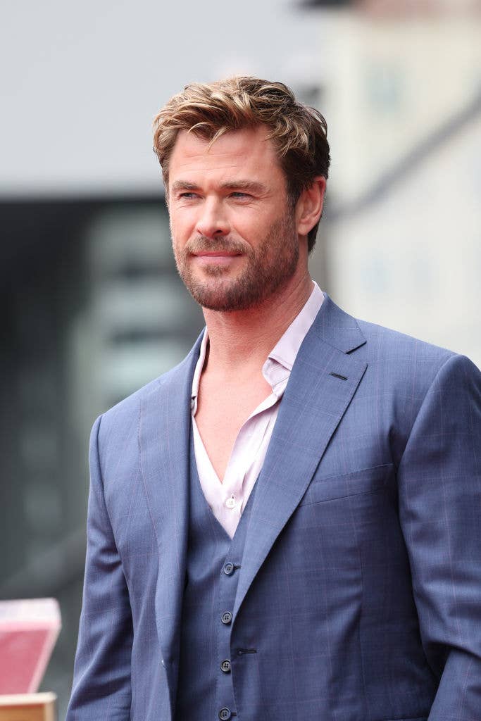 Chris Hemsworth in a three-piece suit with an open-collar shirt, posing on a red carpet