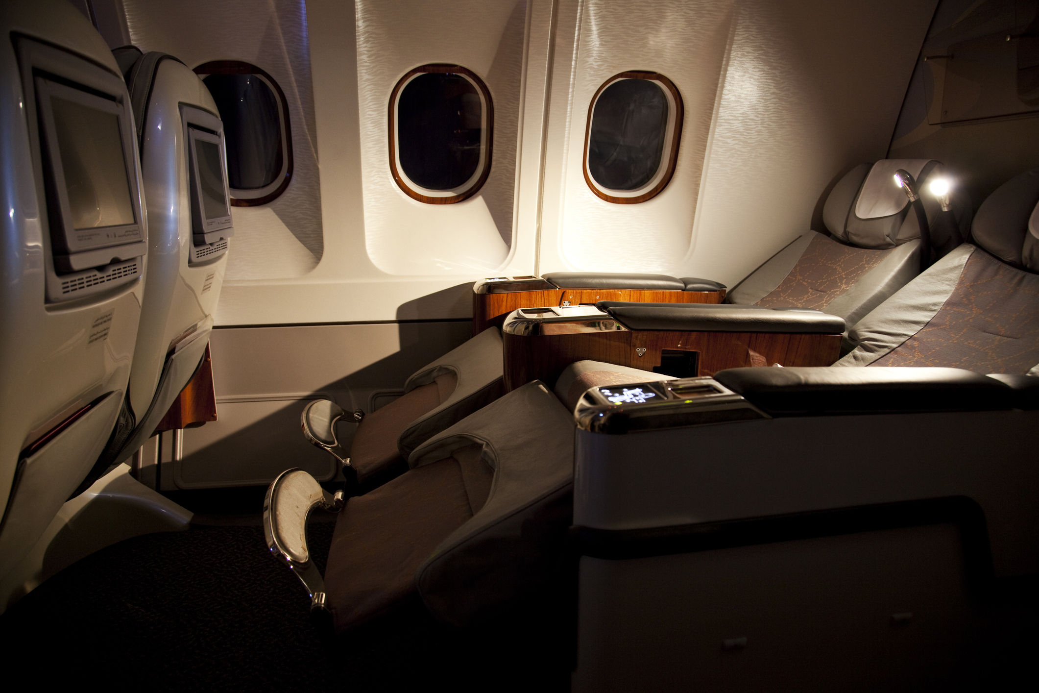 Luxury airplane first-class cabin with reclining seats, entertainment screens, and ambient lighting