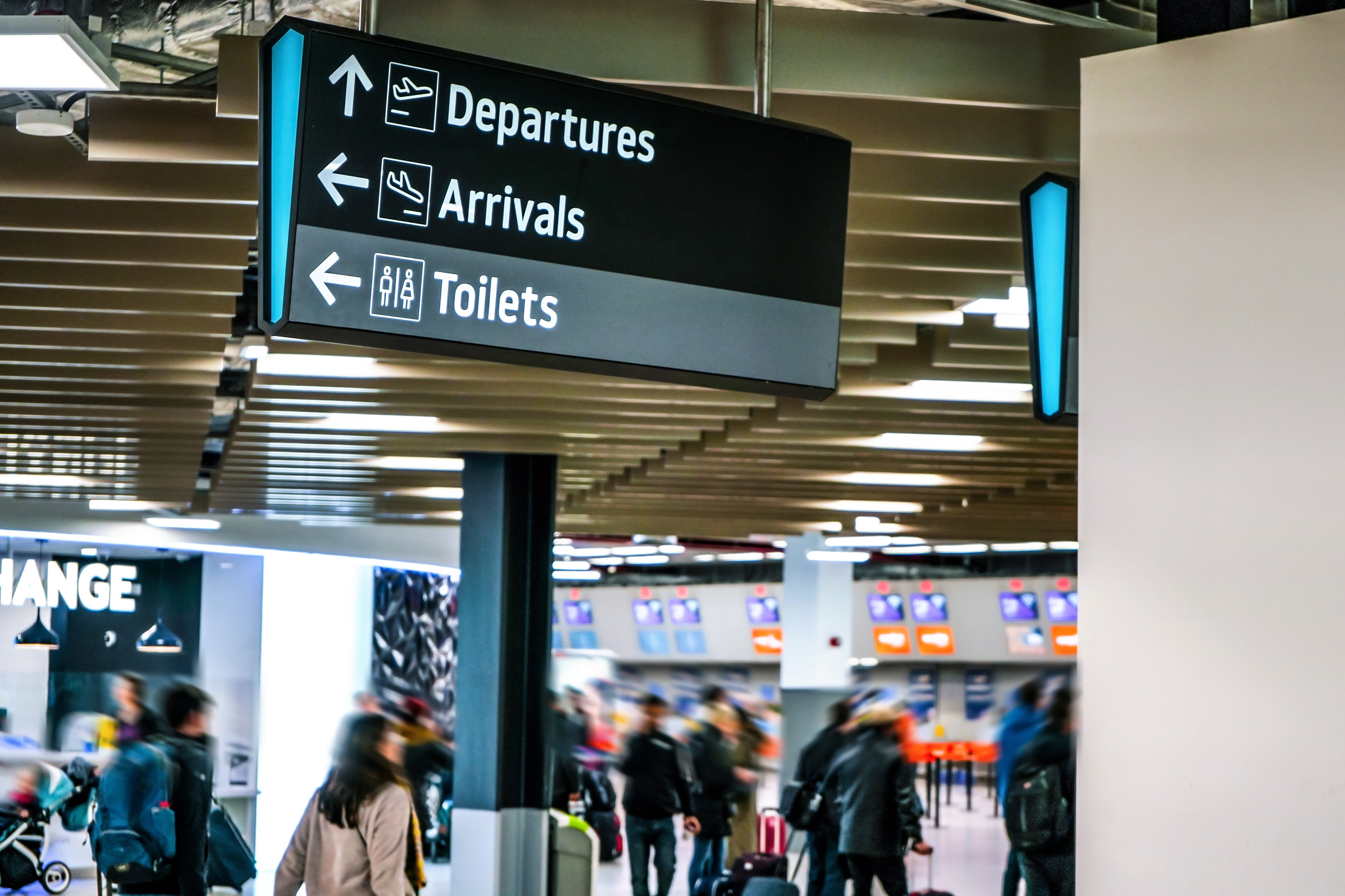 Airport terminal with people walking and signs indicating directions for Departures, Arrivals, and Toilets