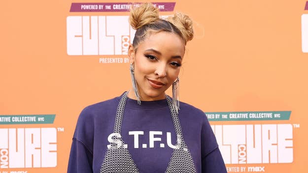 Tinashe poses at an event wearing a sweatshirt with "S.T.F.U." on it, paired with a metallic mesh top