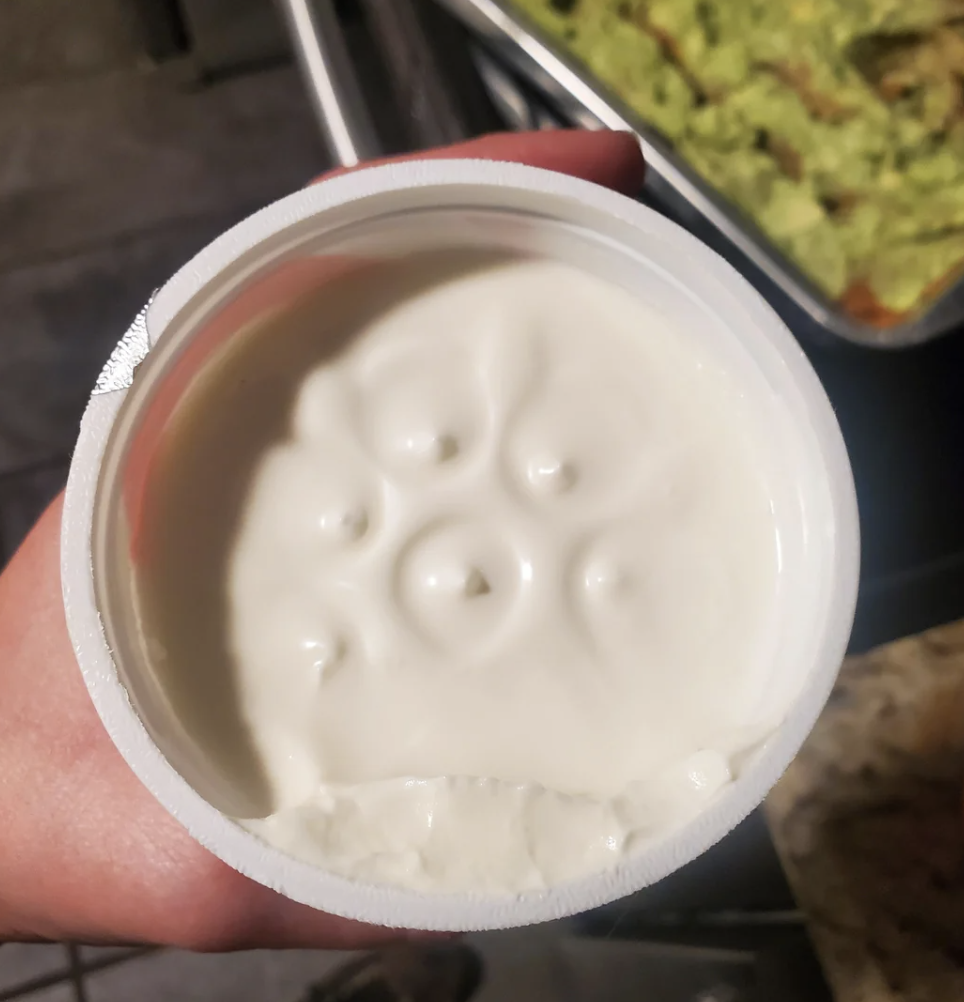Close-up photo showing a round tub of sour cream with an indentation pattern left by the filling machine. Text around the image discusses the pattern's origin