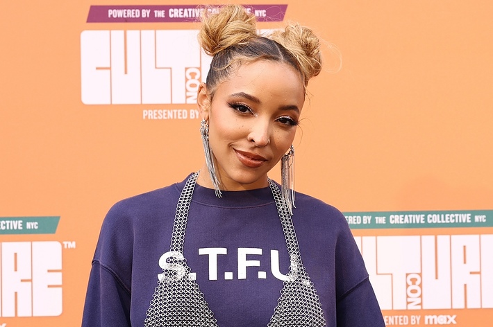 Tinashe on the red carpet at CultureCon, wearing a shirt with "S.T.F.U" text and large dangling earrings