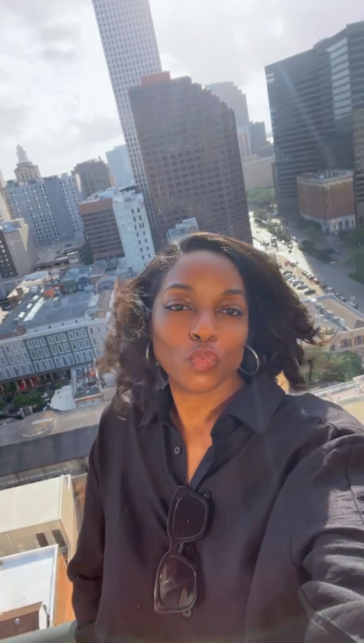 Woman taking a selfie with a cityscape backdrop, featuring tall buildings