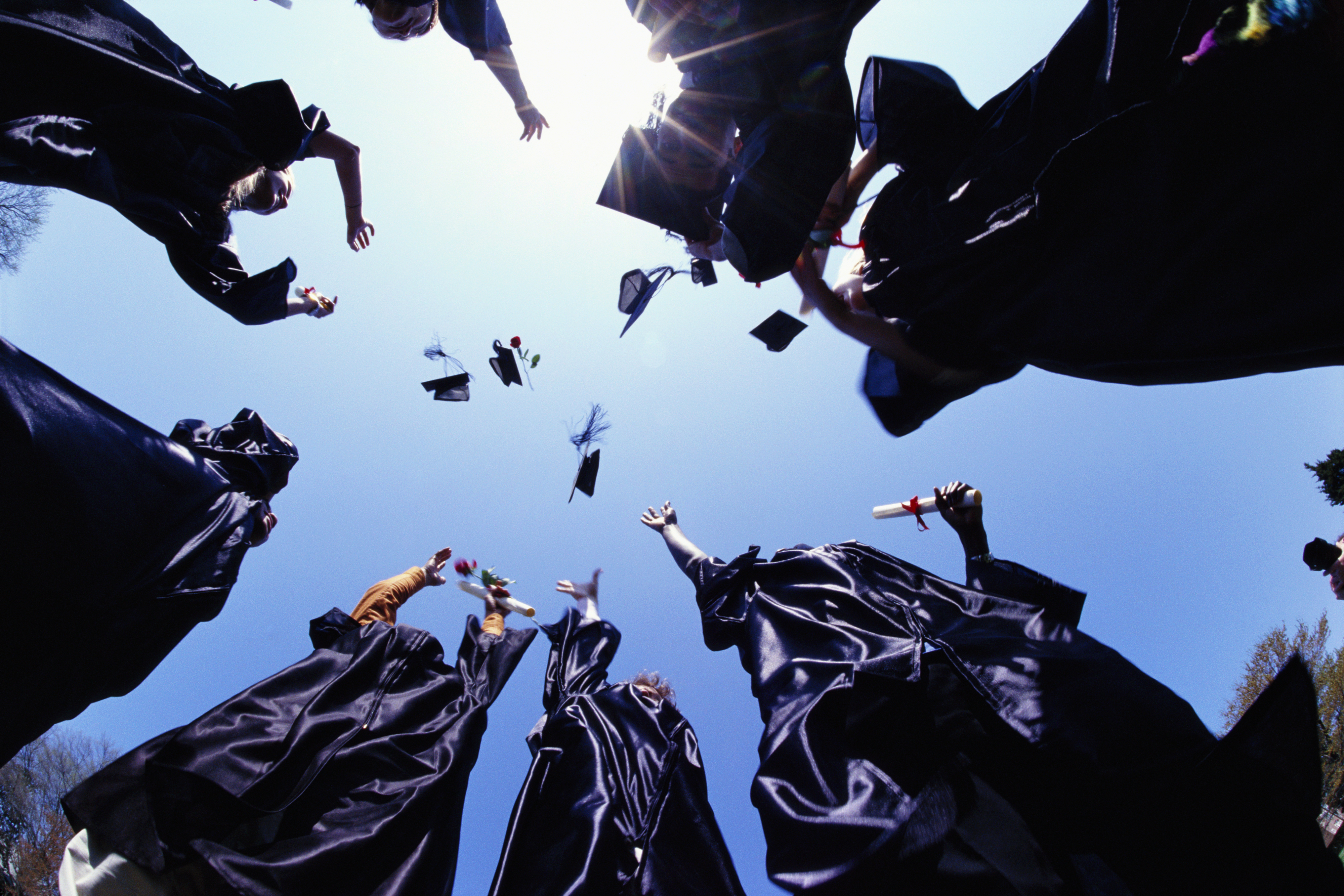 Graduates in gowns toss caps into the sky in celebration against a clear blue backdrop