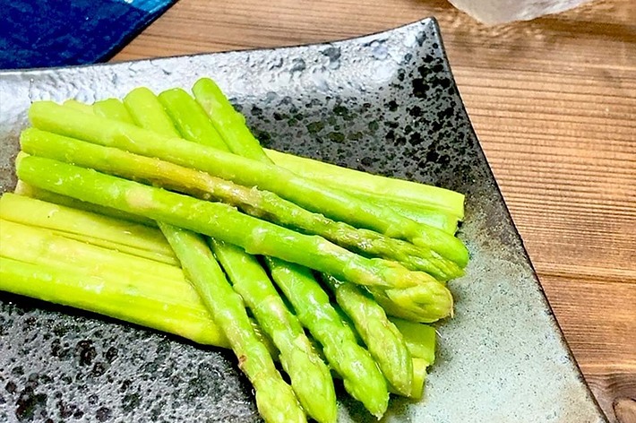 焼きアスパラガスが盛り付けられた四角い皿。背景に箸と一緒にガラスの容器。