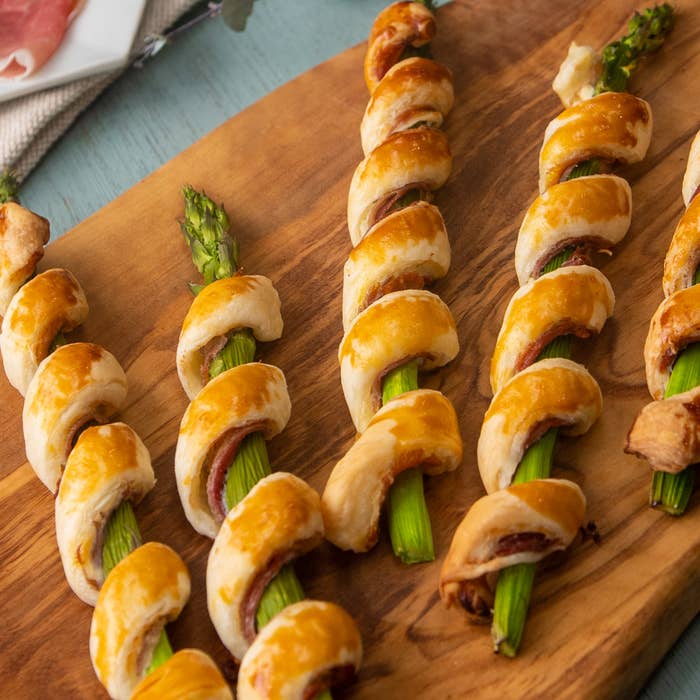 アスパラガスにパイ生地が巻かれ、焼かれた料理が木製のプレートに並んでいる。