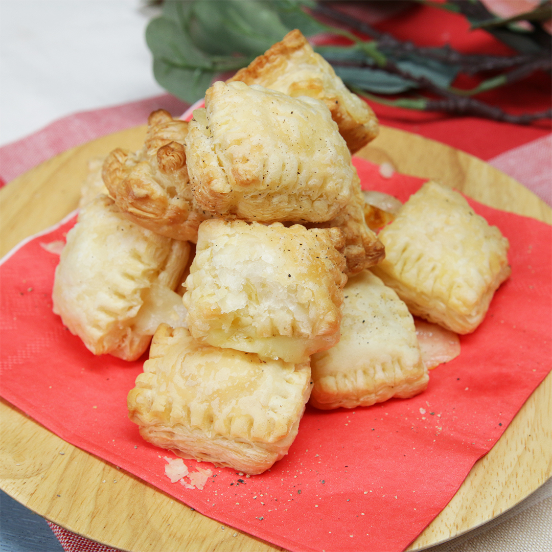 山盛りの焼き立てのチーズパイが木製の皿の上に積まれている。背景には花が少し見える。