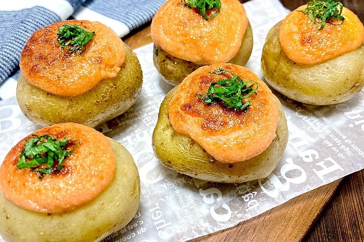 紙の上にのった4つのポテトで、トマトソースとハーブがトッピングされています。クロスも一部見えます。