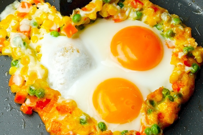 フライパンにあるハート型の野菜入り目玉焼き。