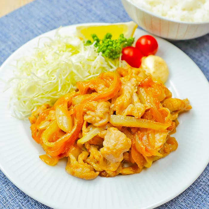 炒め物が盛られたお皿、横には千切りキャベツ、プチトマト、パセリとご飯の入ったおわんが置かれています。