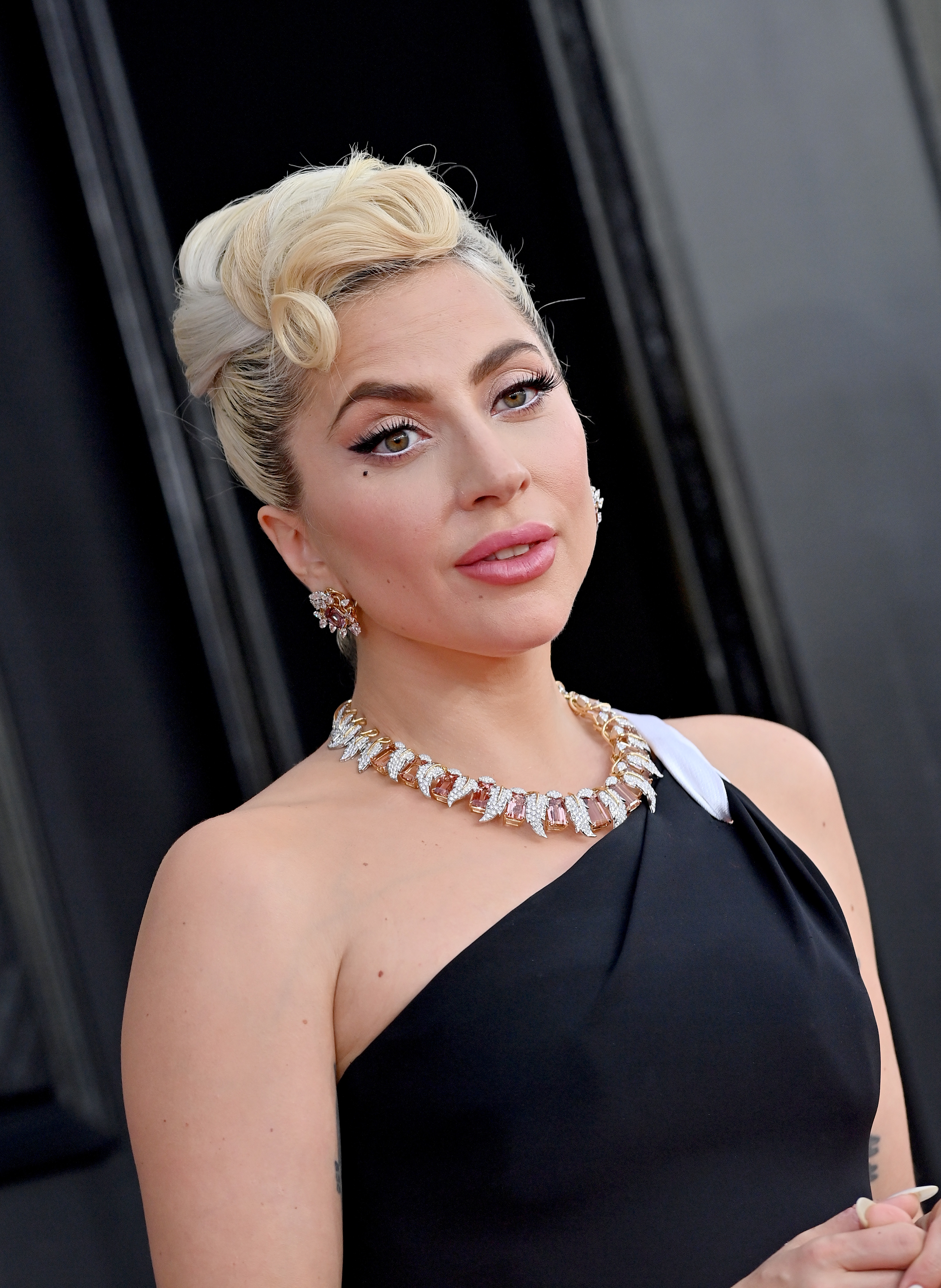 Lady Gaga wears an elegant one-shoulder dress with a statement necklace and earrings at a formal event