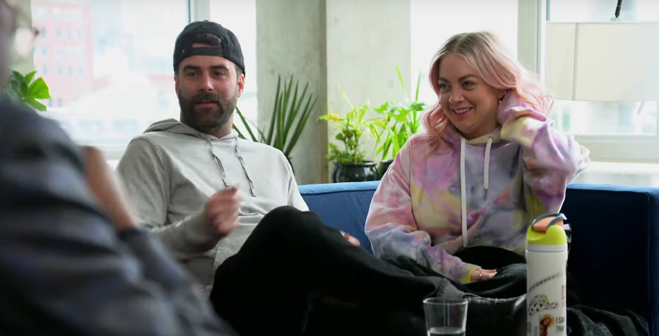 Becca and Austin from "Married at First Sight, S17, E18" are sitting on a couch and having a conversation. Austin is wearing casual clothes