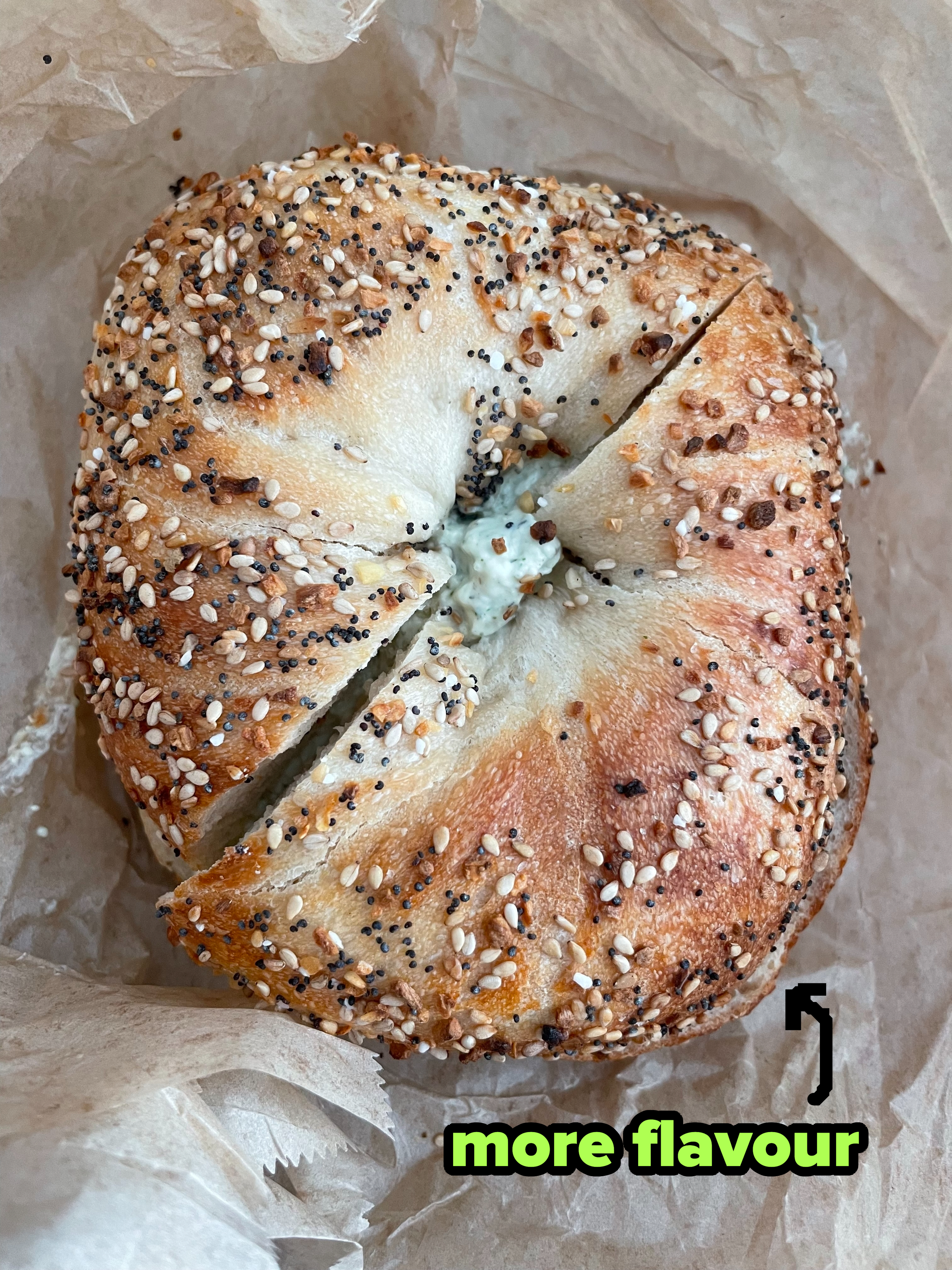 Close-up of a bagel with sesame and poppy seeds, sliced in half and filled with cream cheese, placed on crinkled parchment paper