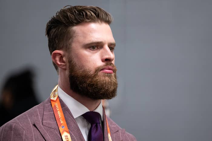 Harrison Butker with a full beard and short hair wears a formal suit with a tie, with a lanyard around his neck