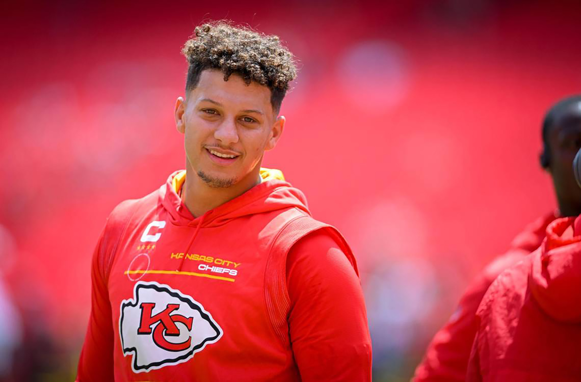 Patrick Mahomes, wearing a Kansas City Chiefs hoodie, smiles at the camera