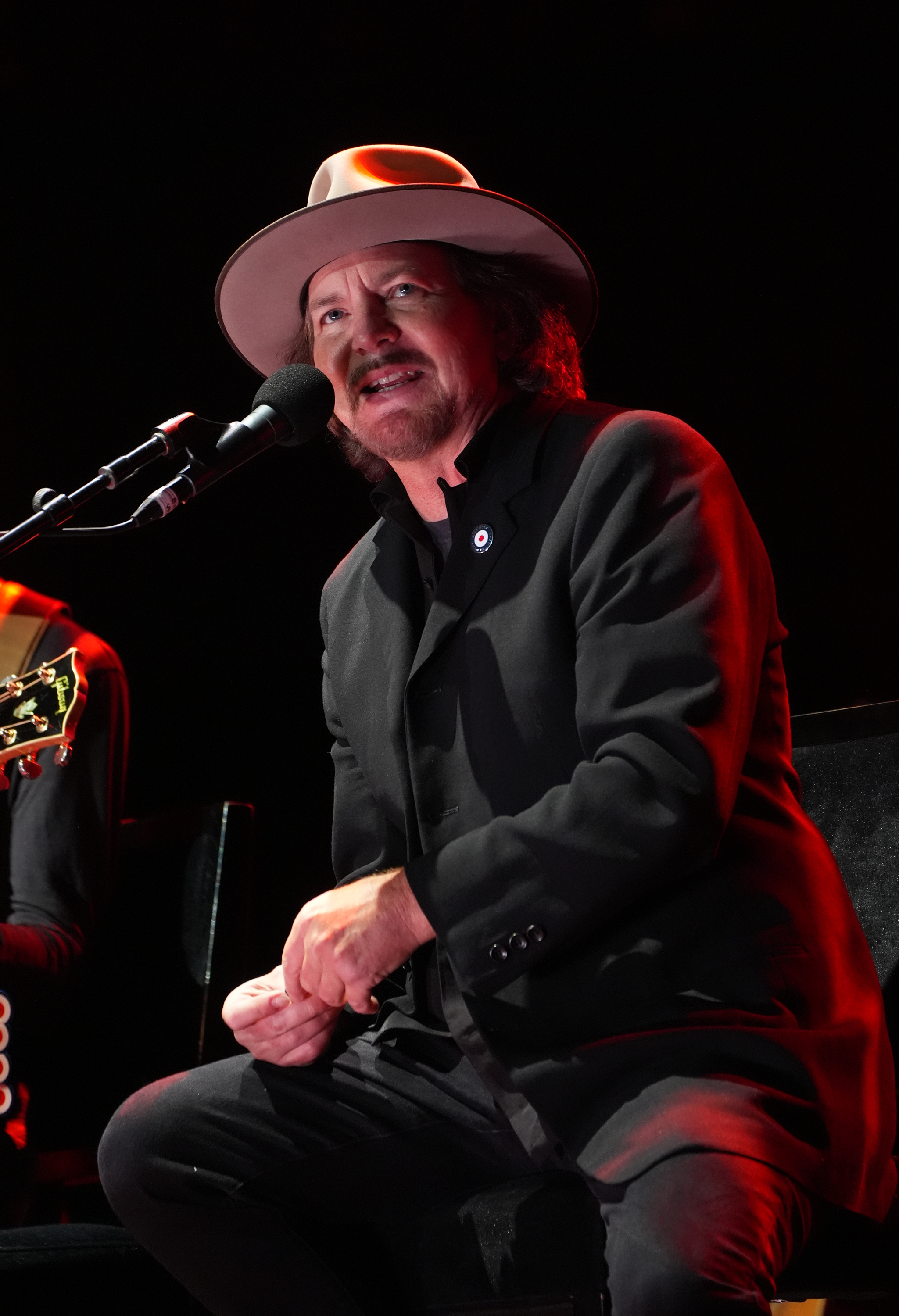Eddie Vedder performs on stage, wearing a dark jacket and a wide-brimmed hat