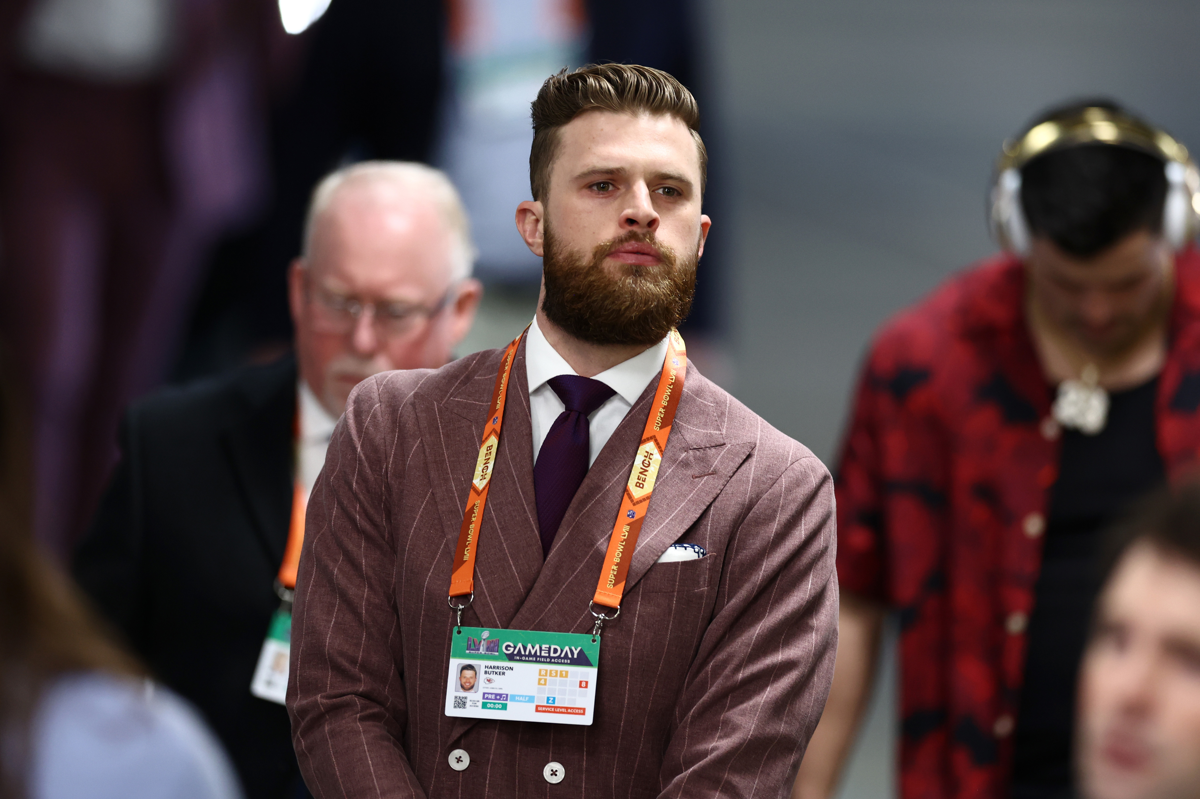 Harrison Butker sporting a full beard, wearing a striped suit and a tie, has a lanyard around his neck at an event