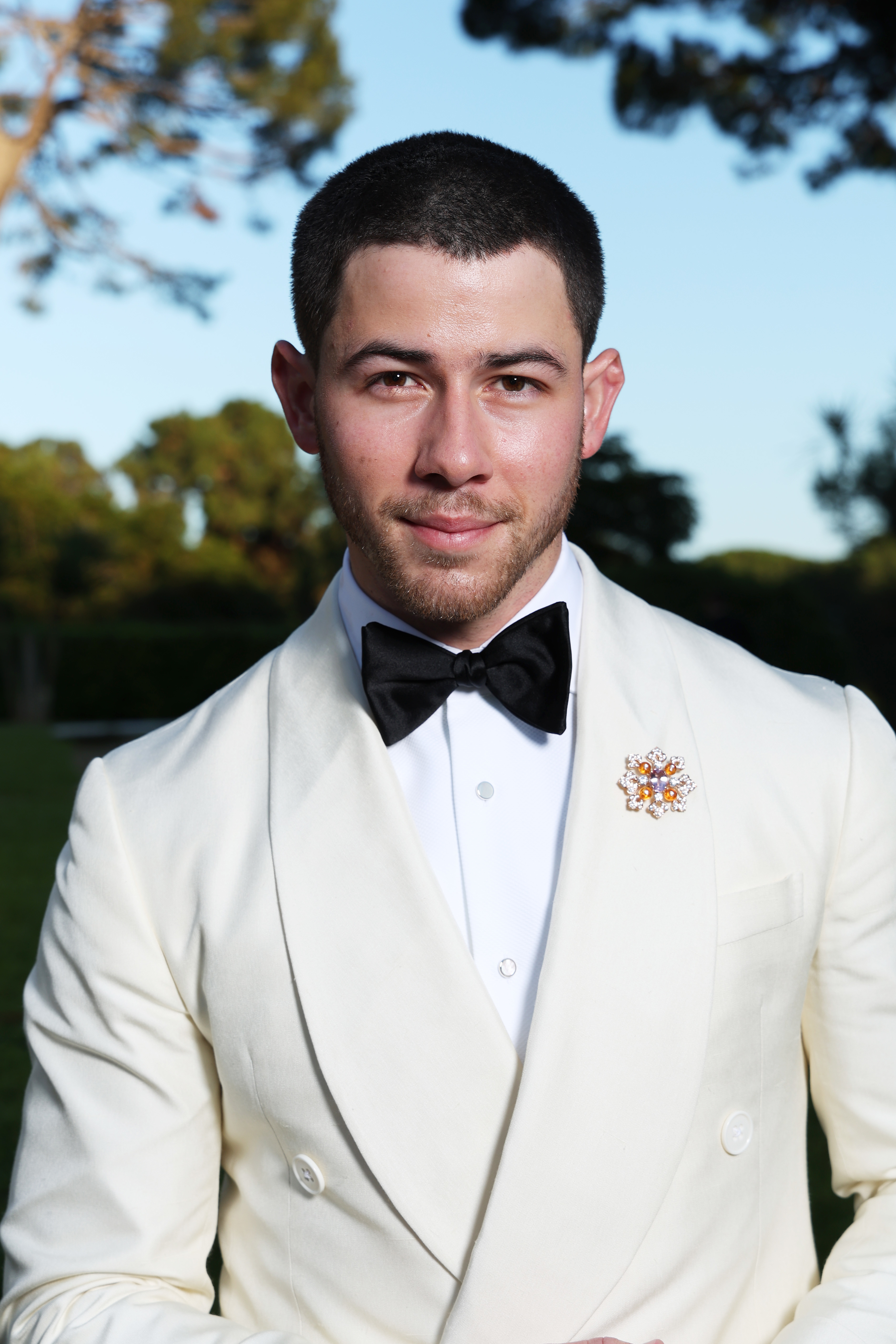 Nick Jonas in a white suit with a black bow tie at an outdoor event