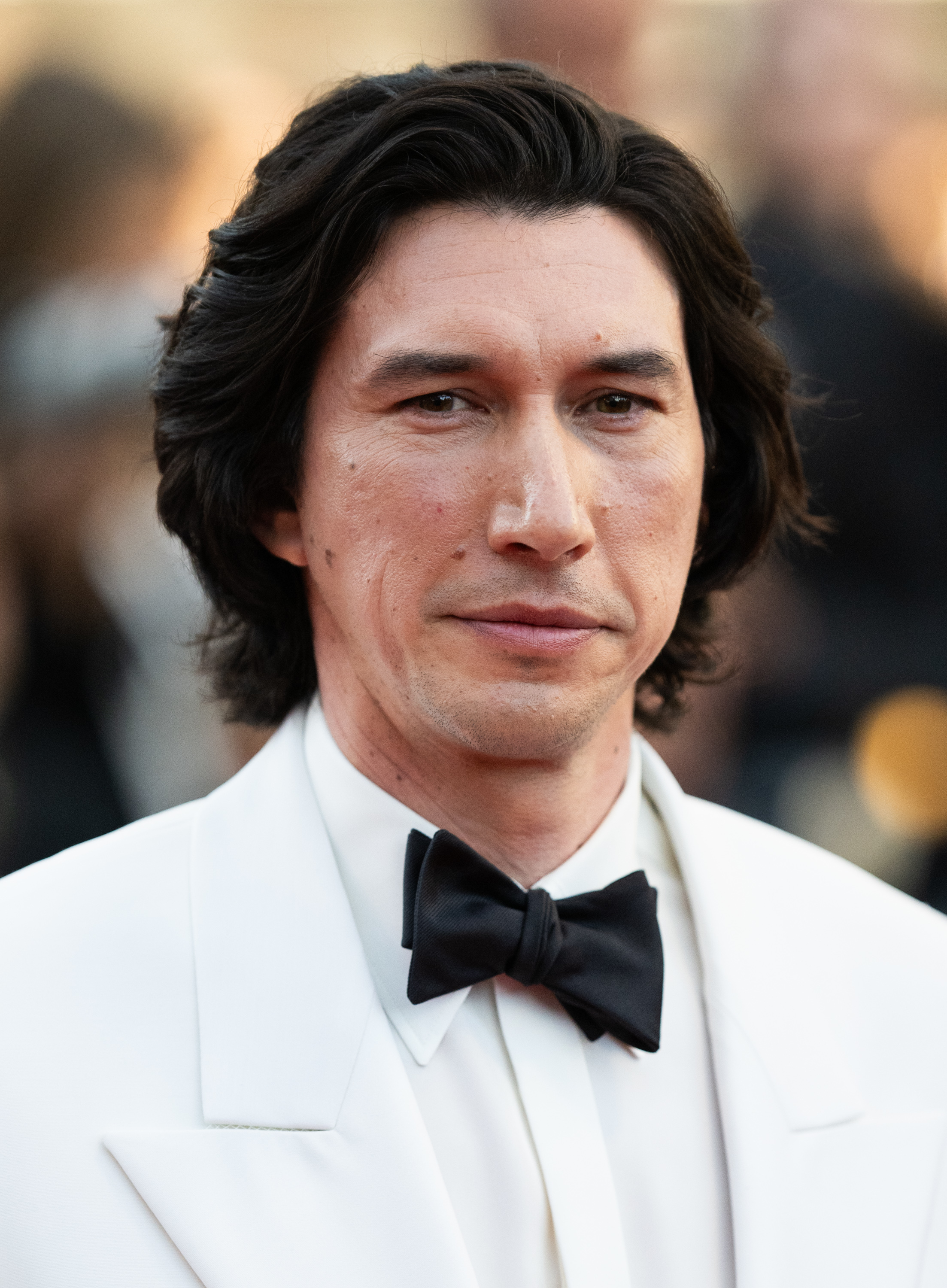 Adam Driver wearing a white tuxedo with a black bow tie at a red carpet event