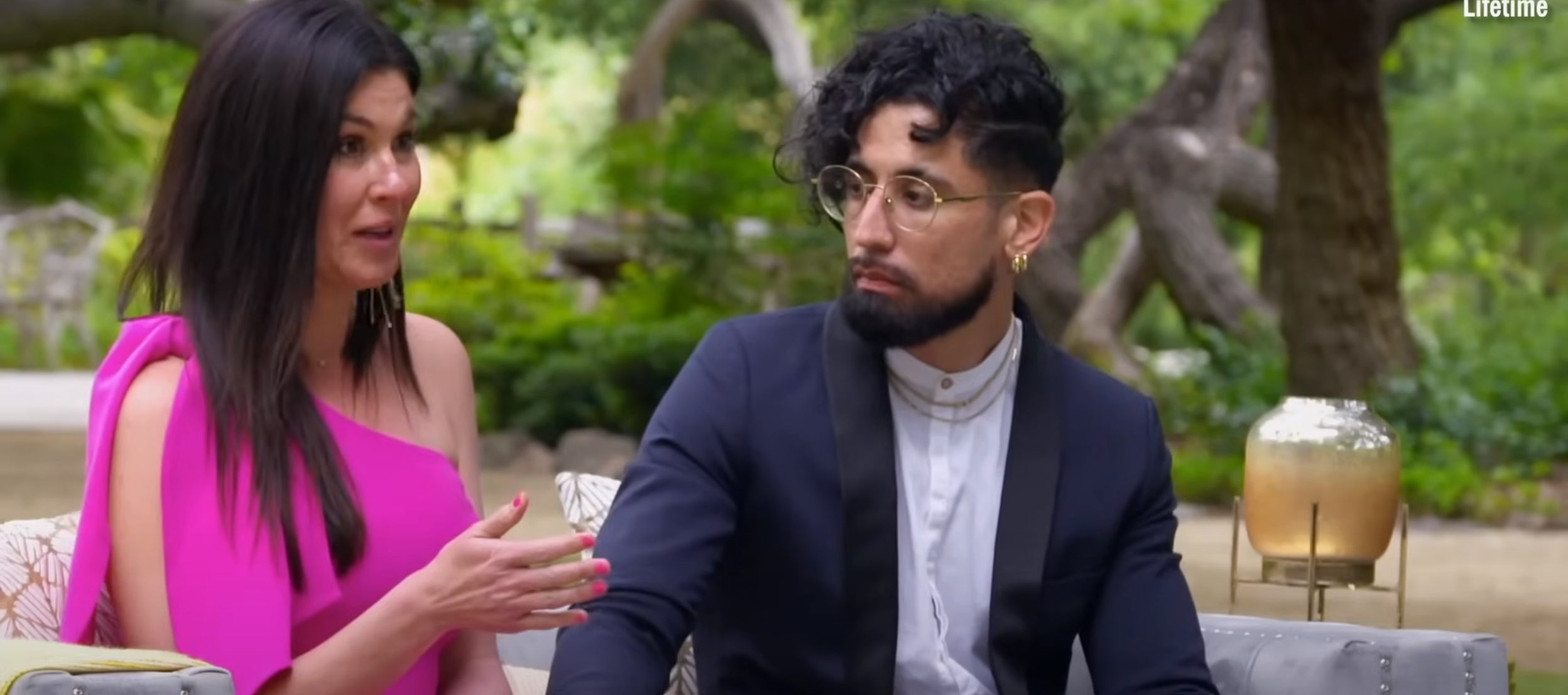 Michael and Chloe from 'Married at First Sight' sit together on an outdoor couch, having an emotional conversation. Michael wears a dark suit; Chloe wears a pink dress