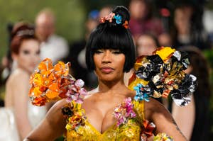 Nicki Minaj at a red carpet event, wearing a vibrant, floral-themed dress with large, shiny flower embellishments on the sleeves and bodice
