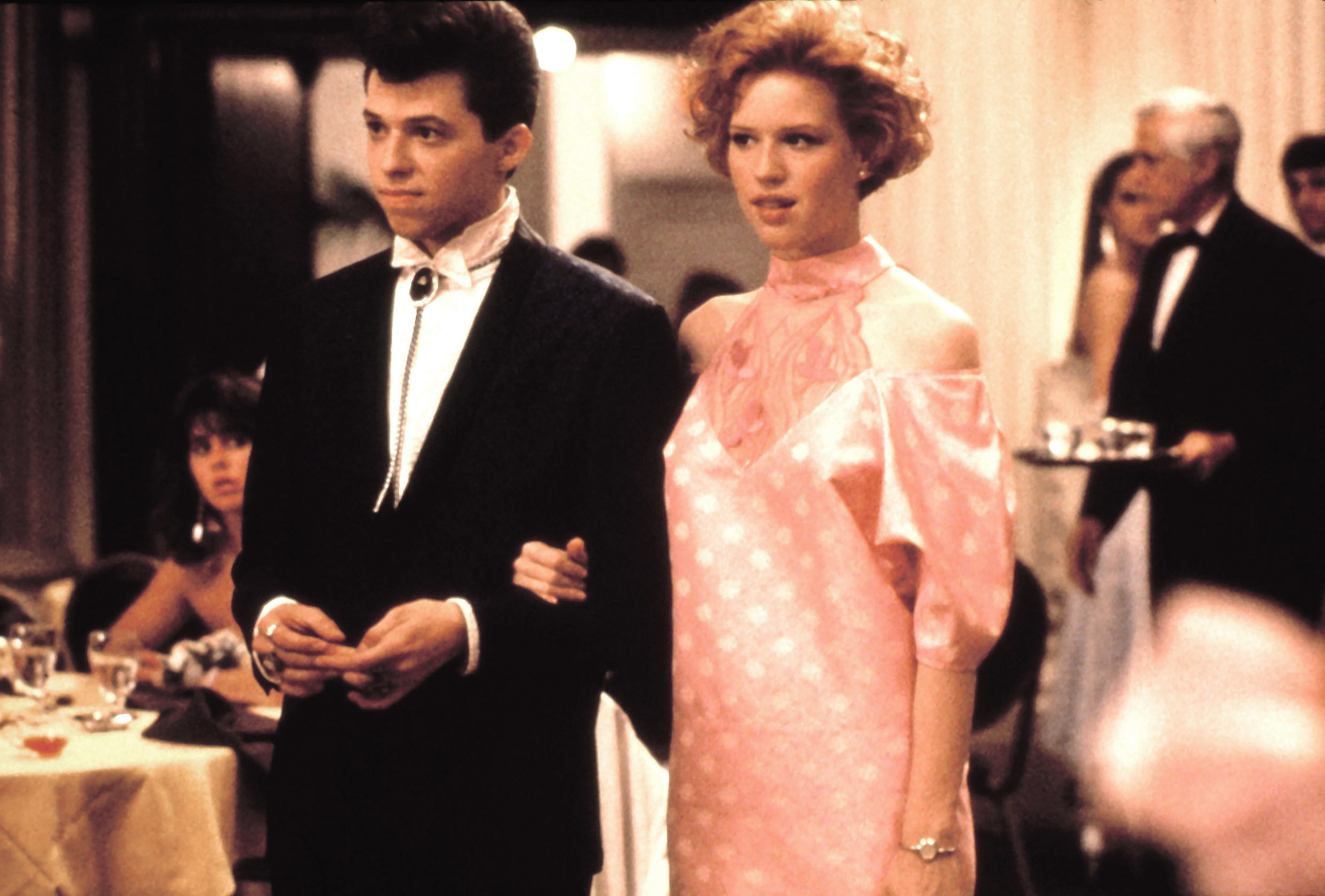 Jon Cryer in a tuxedo with bolo tie and Molly Ringwald in a pink off-shoulder dress at a formal event